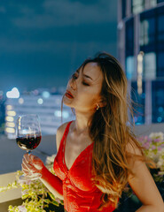 Portrait of beautiful young Asian woman enjoying loneliness and solitude with a glass of wine at rooftop bar and restaurant at night. Lifestyle and nightlife concept.