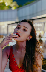 Fototapeta premium Sexy brunette asian woman tipsy in red dress blowing cigarette smoke on blurred cafe background at night.