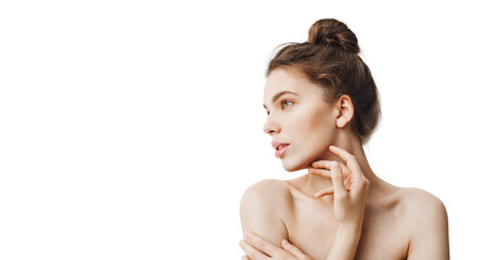 Fototapeta premium Portrait of young female brunette with bun hairstyle and baked shoulders looking aside with calm face expression touching jawline with fingers. Beauty and health skincare sale banner and promos design