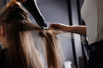 hairdresser drying hair with hair dryer and comb in beauty salon, drying hair close-up