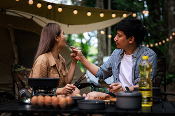 close up and  of young asian woman and couple sitting grilled meat in pan  picnic gas in the camping ground. concept the weekend vacation his and her.