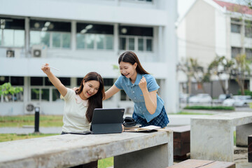 Fototapeta premium Two Excited Female Students Celebrating Success While Studying Outdoors with a Tablet at a Modern Campus