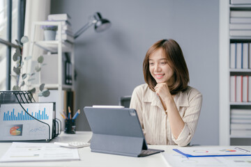 Young Professional Woman Working on Tablet in Modern Office with Charts and Graphs on Desk