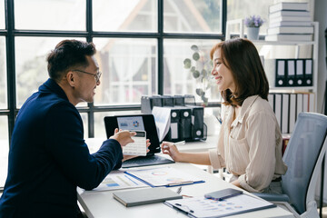 Business Meeting in Modern Office with Two Professionals Discussing Documents and Charts by Large Window