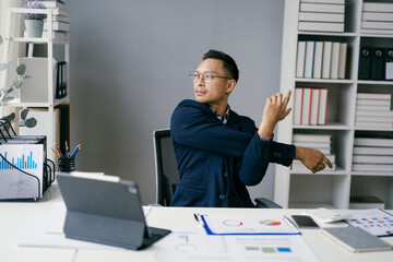 Business Professional Stretching at Desk in Modern Office with Documents and Digital Devices