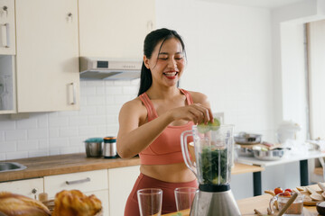 Woman in Athletic Wear Preparing a Healthy Smoothie in a Modern Kitchen with a Blender