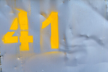 Metal sheet painted with gray color with yellow spray painted number 41. Empty deformed metal wall...