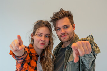 Young couple or friends, a man and woman in casual clothing, pointing directly at the camera with engaging expressions