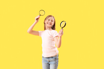Little girl with magnifiers on yellow background