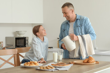 Little girl and her father with different pastries drinking milk at table in kitchen