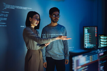 Asian Two software developers engaged in collaborative coding session, with code projected onto the wall and multiple computer screens displaying