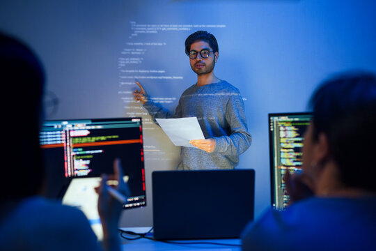 asian developer leads present code review session, pointing at code projected on the wall with colleagues  teamwork and knowledge sharing in software development.