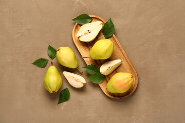 Wooden board with fresh pears and leaves on brown background