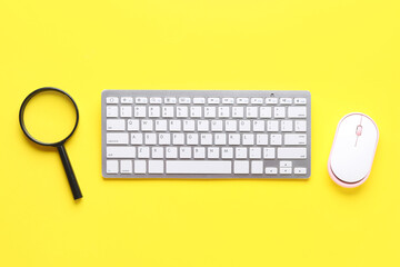 Modern computer keyboard with mouse and magnifier on yellow background