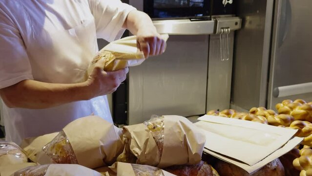 The process of packaging dough products in a bakery. The baker packs the bread fresh from the oven in eco paper bags. The working process of a successful bakery business