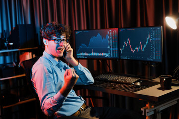 Successful business trader calling on smartphone with raising fist up of highest profit on global market online in real time at neon modern office. Concept of dynamic stock exchange growth. Gusher.