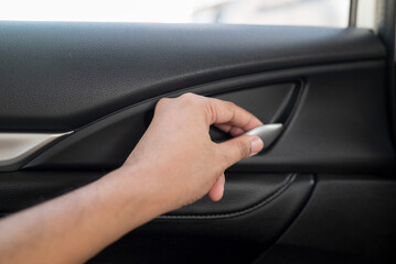 A hand reaching to open a car interior door handle against the backdrop of a black car door panel....