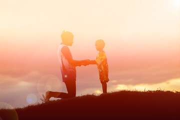 a silhouette of a happy young girl child the arms of his loving mother for a hug, in front of the sunset in the sky on a summer day.