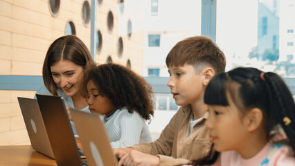 Smart teacher teaching and looking student using laptop at classroom. Professional instructor...