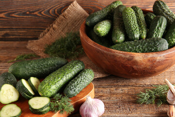 Board and bowl with fresh cucumbers on wooden background
