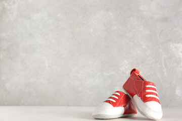 Stylish baby shoes on white table near grunge grey wall