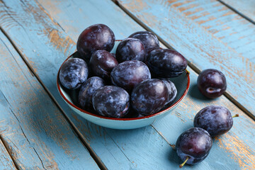 Bowl with fresh plums on blue wooden background