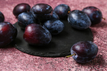 Black board with fresh plums on purple background