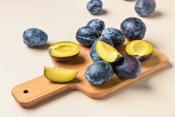 Wooden board with fresh plums on beige background