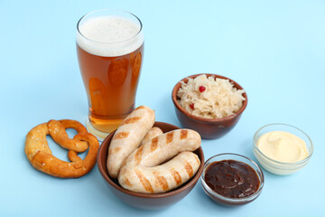 Bowls with tasty Bavarian sausages, pretzel, sauces, sauerkraut and glass of beer on blue background. Oktoberfest celebration