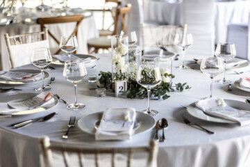 A wedding table covered with a white tablecloth, decorated with flowers, candles, glasses and cutlery.
