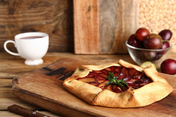 Board of delicious plum galette with mint on wooden background