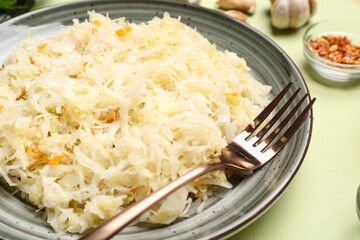 Plate with tasty sauerkraut with spices on green background