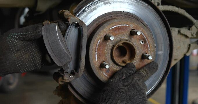 Auto mechanic showing uneven brake pad wear on an old brake disc, work process of inspecting car parts at a technical inspection station