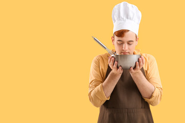 Male confectioner in apron with bowl and whisk preparing tasty meringue on yellow background