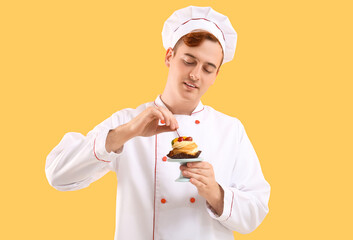 Male confectioner in uniform with tasty profiterole on yellow background