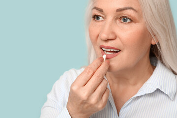 Beautiful mature woman taking pill on blue background
