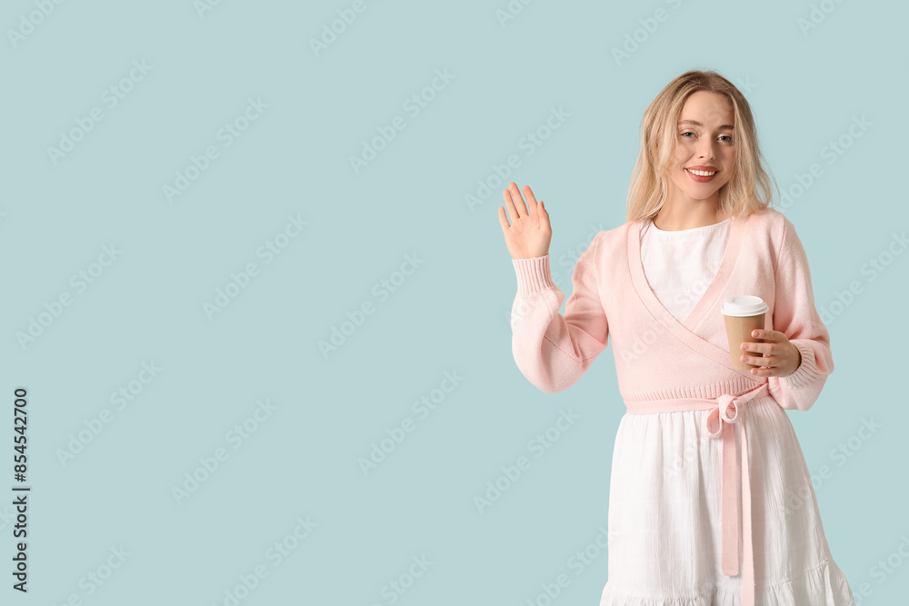 Poster Beautiful young woman with cup of coffee waving hand on blue background