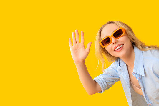 Young beautiful woman waving hand on yellow background
