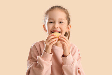 Cute little girl with cookie on beige background