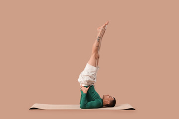 Young man doing yoga on mat against brown background