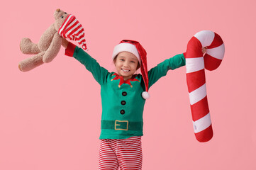 Cute little girl with teddy bear and Christmas cushion on pink background