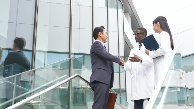 Businessmen and a group of multinational engineers in white coats shaking hands in a lobby