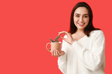 Happy young woman with cup of hot mulled wine on red background