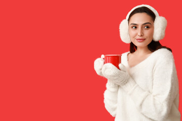 Beautiful young woman in warm mittens with cup of hot mulled wine on red background