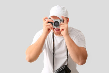 Handsome young happy male tourist with camera taking photo on grey background