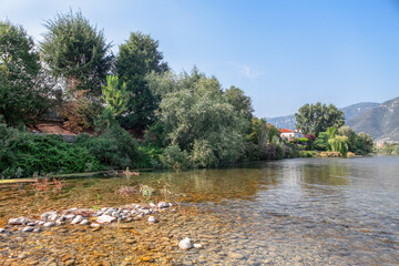 Landscape with mountain and Brenta river in Italy. Serene river flowing amidst rocky terrain and lush trees on the shore