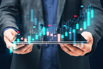 Close up of businessman hands holding tablet with glowing blue candlestick forex chart on blurry background. Financial growth, stock and exchange concept.