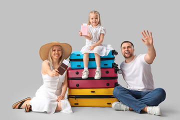 Little girl sitting on suitcases near her parents on grey background