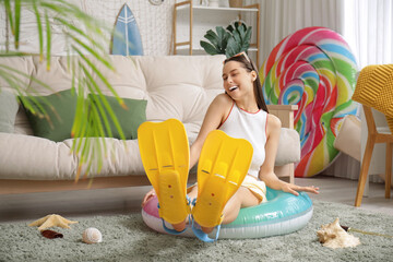 Young pretty woman in flippers and sunglasses sitting on inflatable ring in living room