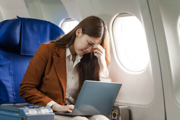 A young Asian woman is sitting in her seat as an airplane passenger, experiencing airsickness with...